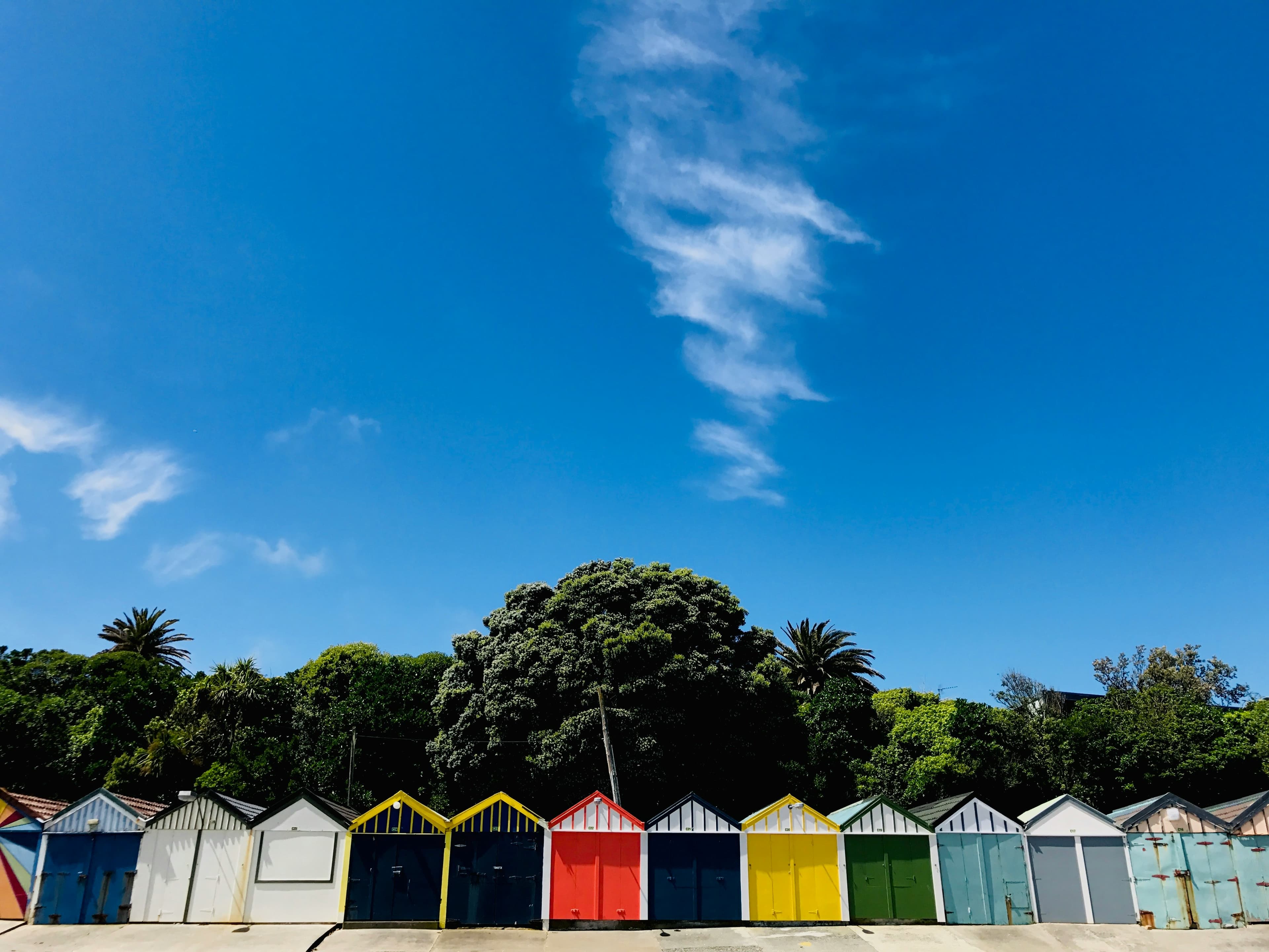 A row of colorful beach huts against a clear blue sky with greenery in the background.